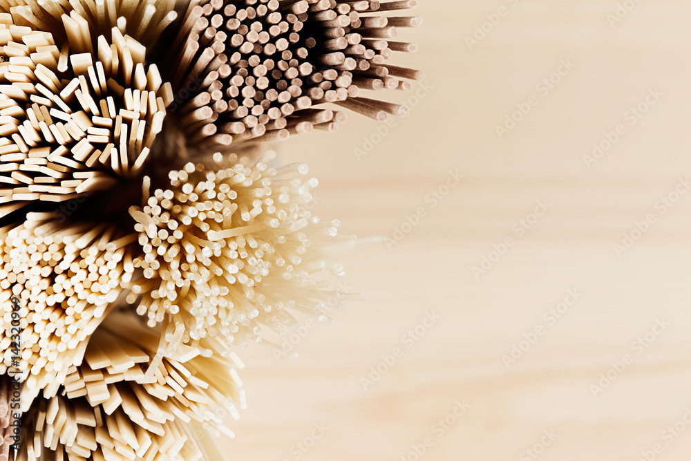 Fototapeta premium Section of raw asian noodles top view close up on soft beige wooden board.