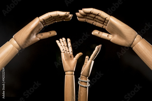 Two giant hands threaten or protect a group of men and women. Isolated on black background. Studio Shot.