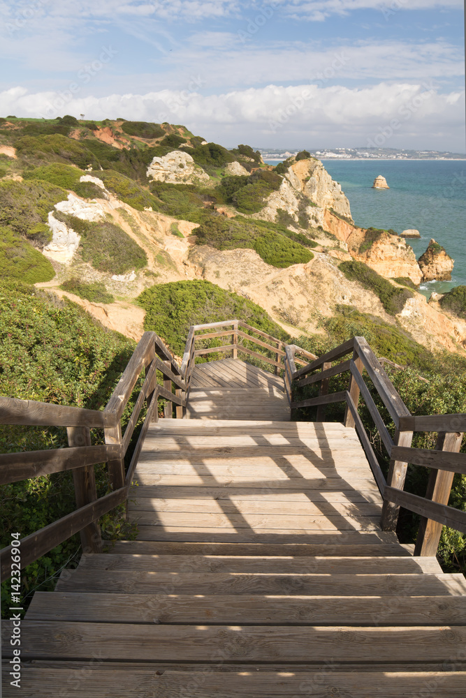 walking down on footbridge to camilo beach cliffs and sea caves, algarve, portugal