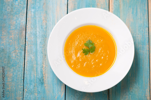 Top view of pumpkin and carrot soup with cream and parsley on blue  wooden background.