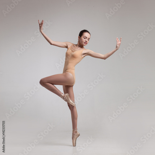 young beautiful ballet dancer in beige swimsuit posing on pointes on light grey studio background © Aleksandr Doodko