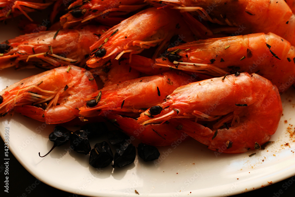 Freshly prepared shrimps lie on a white plate, adorned with spices and lemon. Freshly prepared shrimps lie on a white plate, adorned with spices and lemon.