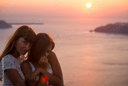 Mother and daughter at sunset. Sunset on the island of Santorini. Girl tourist on a background of the sea and the setting sun. Mother and daughter travel, Mother's love, Girl teenager and her mom. 