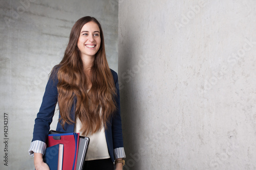 happy student woman holding books folders and laptop under her arm