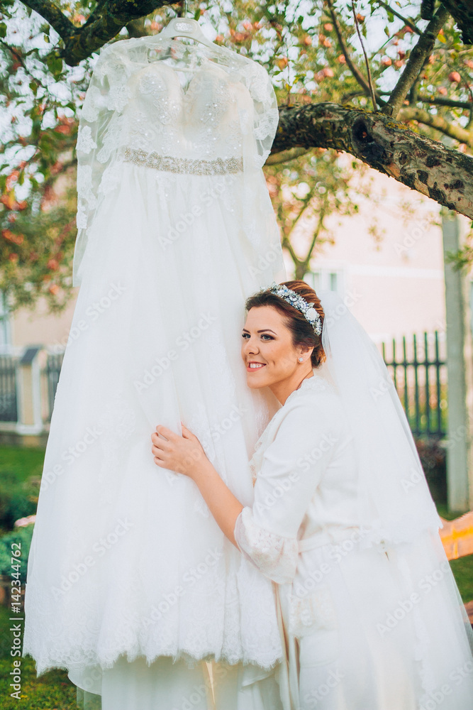 Bride in robe near wedding dress on tree outdoor in the garden backyard house. Bride in robe near wedding dress on tree outdoor in the garden backyard house.