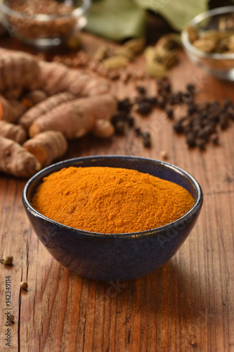 Ground turmeric powder in a bowl on wooden background. Healthy spice.