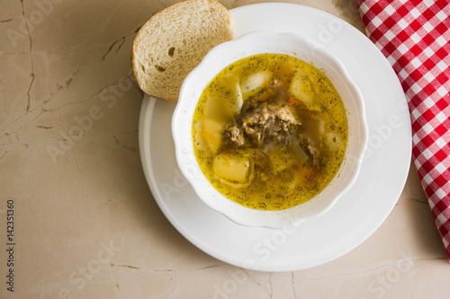 Soup with meat in a white bowl on a marble table. Tasty and nutritious dish.