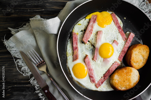 Fried eggs with ham in a frying pan on a wooden table in rustic style