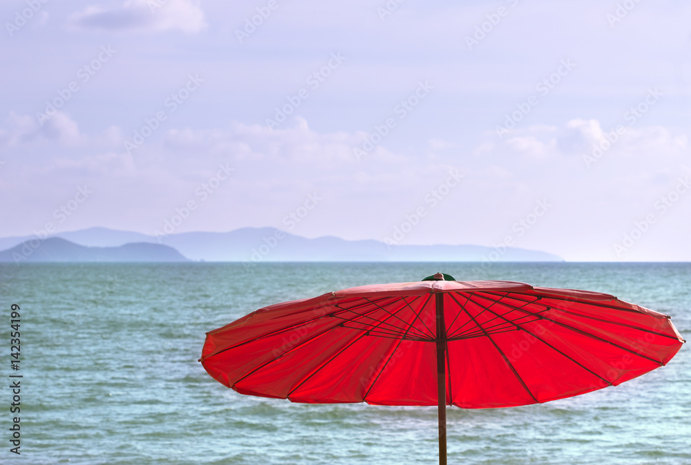 Яркий красный зонт на фоне моря,неба и гор