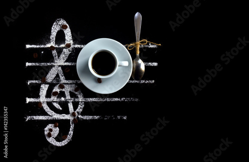 Black coffee in a cup with a spoon on a black background as a concept of musical notes