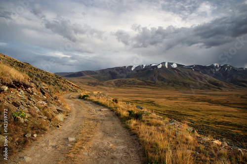 Extreme rocky road in a mountain valley to the pass in cloudy weather on the background of snowy mountain ranges Plateau Ukok Altai Siberia Russia