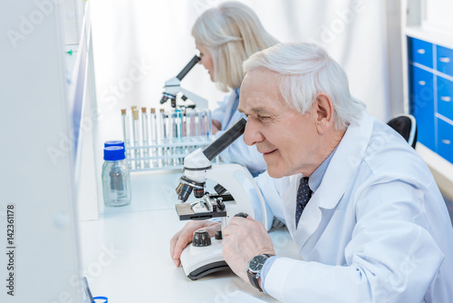 smiling senior chemists with microscope in laboratory