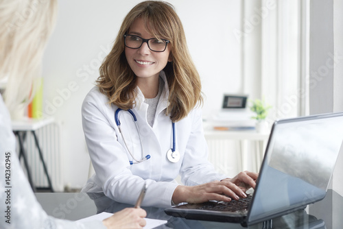 Doctor and her patient. Shot of a middle aged female doctor sitting in front of laptop and consulting with her patient.