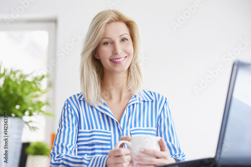 Businesswoman in the office. Portrait of a smiling blond businesswoman doing some paperwork and working on laptop.