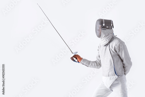 side view of fencer in uniform training with rapier on white