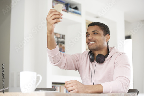 Take a selfie. Cropped shot of a handsome Afro American young man using his cellphone and taking selfie while chilling at home.