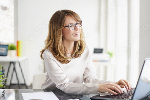 Thinking on business strategy. Portrait of a smiling professional businesswoman doing some paperwork and working on laptop at office.