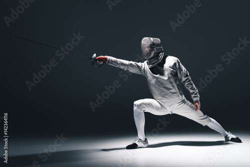 Slika na platnu Professional fencer in fencing mask with rapier standing in position on grey
