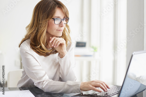 Thinking on business strategy. Portrait of a smiling professional businesswoman doing some paperwork and working on laptop at office.