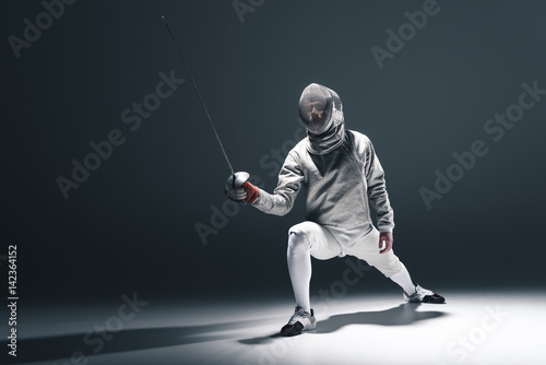 Foto Professional fencer in fencing mask with rapier standing in position on grey