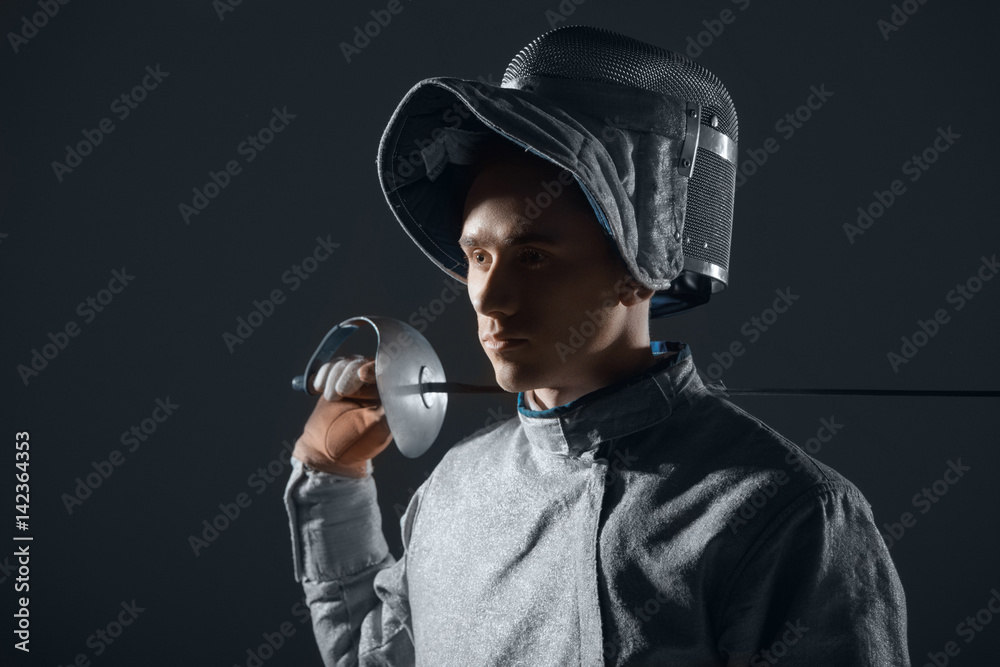 Portrait of professional fencer in fencing mask with rapier on grey Portrait of professional fencer in fencing mask with rapier on grey