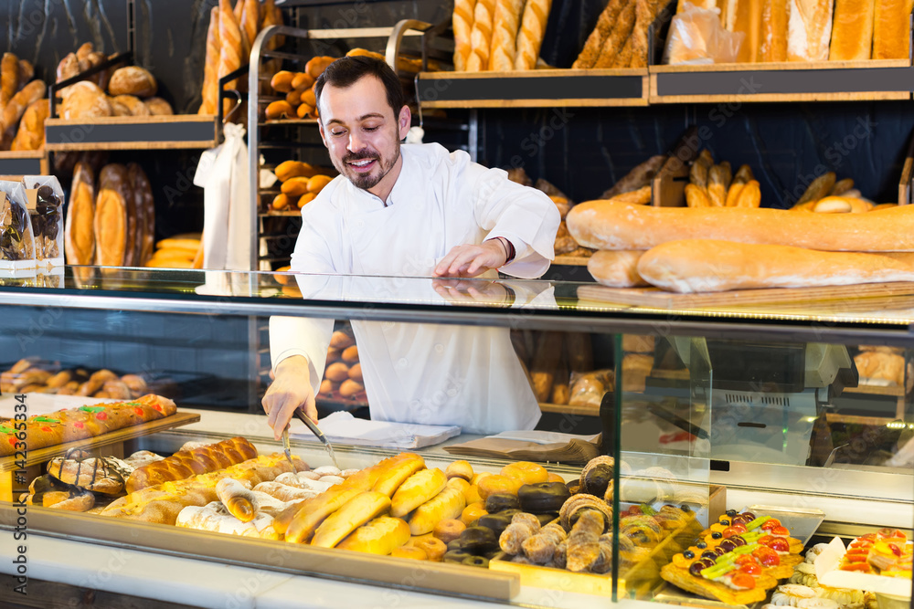 Male shop assistant demonstrating fresh delicious pastry in bakery