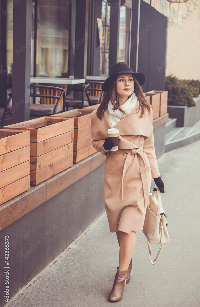 Fototapeta premium Young woman walks in the city with a cup of coffee