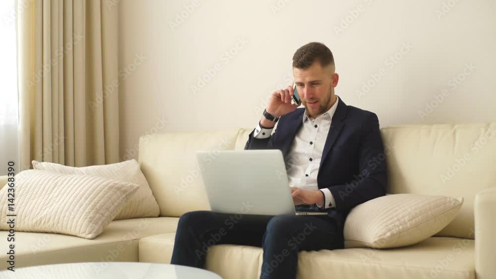Staying in touch with colleagues. Handsome young man in shirt working on laptop and talking on the mobile phone Staying in touch with colleagues. Handsome young man in shirt working on laptop and talking on the mobile phone