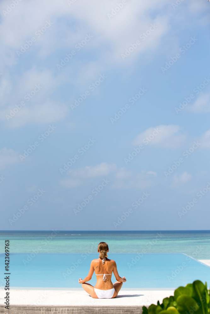 Beautiful girl sits in a pose of a lotus and meditates on the coast Maldives Beautiful girl sits in a pose of a lotus and meditates on the coast Maldives