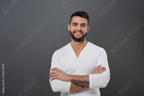 Young handsome man smiling with crossed arms over grey background.