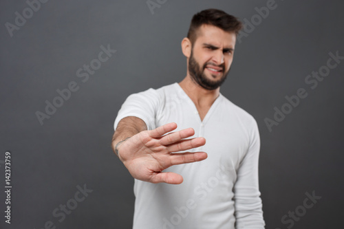 Displeased man refusing, stretching hand to camera over grey background.