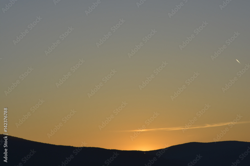 Clear blue orange sky during sundown behind silhouette of hills.