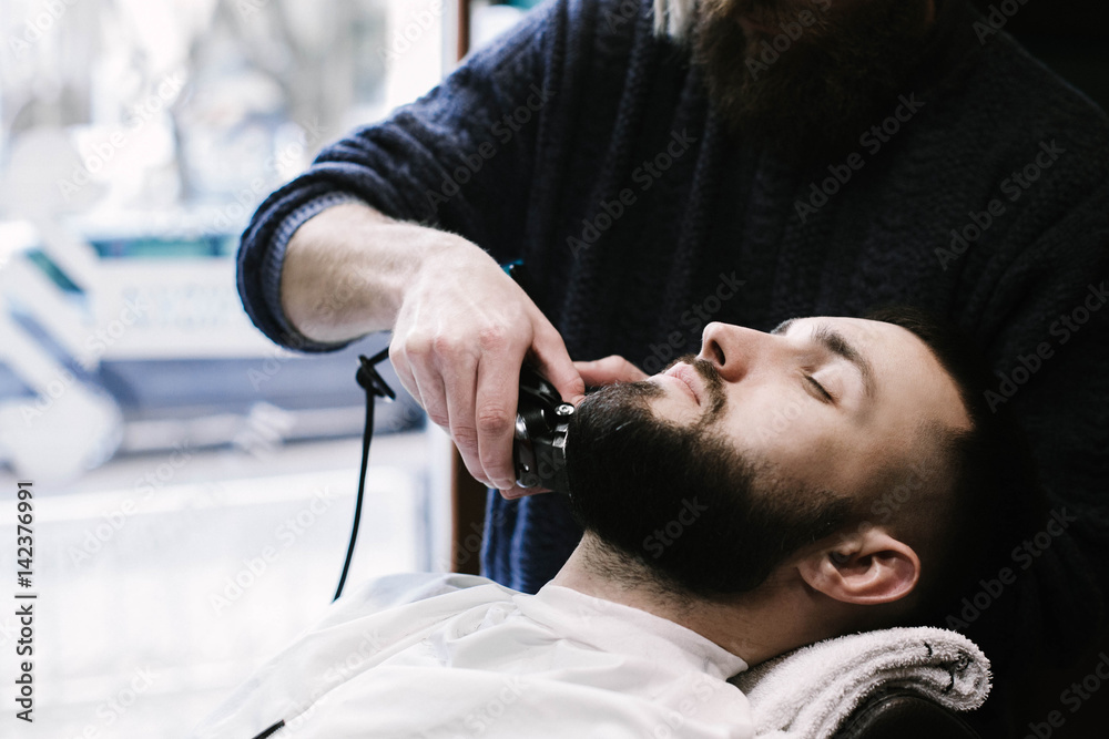 Fototapeta premium Man lies in the chair while barber cuts his beard
