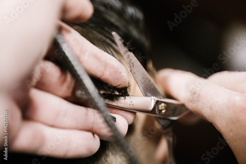 Barber holds man's hair in fingers while he cuts it