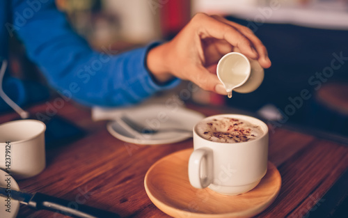 Man hand pouring a syrup onto a hot coffee cup.