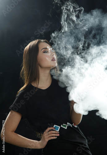 Young girl in a black t-shirt smoking an electronic cigarette (vaping) on a black background