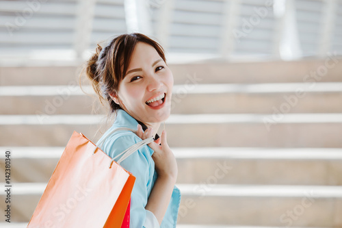 Beautiful asian girl happy and smiling in shopping time holding colorful paper bag, look at camera, color effect filter 