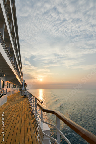Cruise ship wooden promenade deck with beautiful sunset  and reflection on the ocean.