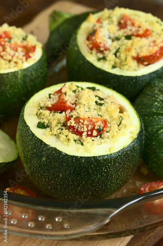 Baked round zucchini stuffed with couscous, cherry tomato and parsley, photographed with natural light (Selective Focus, Focus on the cherry tomato on the first stuffed zucchini)