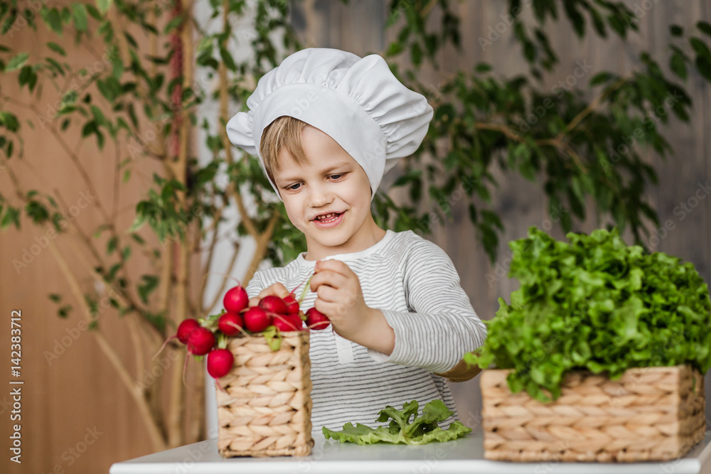 Handsome little kid in chef uniform with vegetables. Cooking in kitchen at home. Vegetarian. Healthy food Handsome little kid in chef uniform with vegetables. Cooking in kitchen at home. Vegetarian. Healthy food