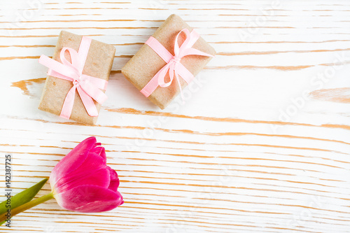 Пара упакованных подарков с розовой лентой и тюльпан на белом деревянном фоне