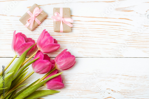 Fototapeta Naklejka Na Ścianę i Meble -  Букет свежих тюльпанов и пара упакованных подарков с розовой лентой на белом деревянном фоне