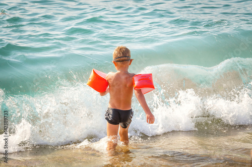 The child runs in the sea to bathe with protective inflatable sleeves
