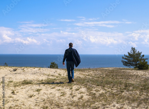 Billede på lærred Young man walking near the beach and looking at sea