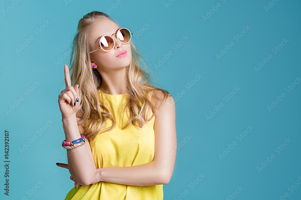 Fototapeta premium portrait of beautiful blond woman in sunglasses and yellow shirt on blue background. Carefree summer.