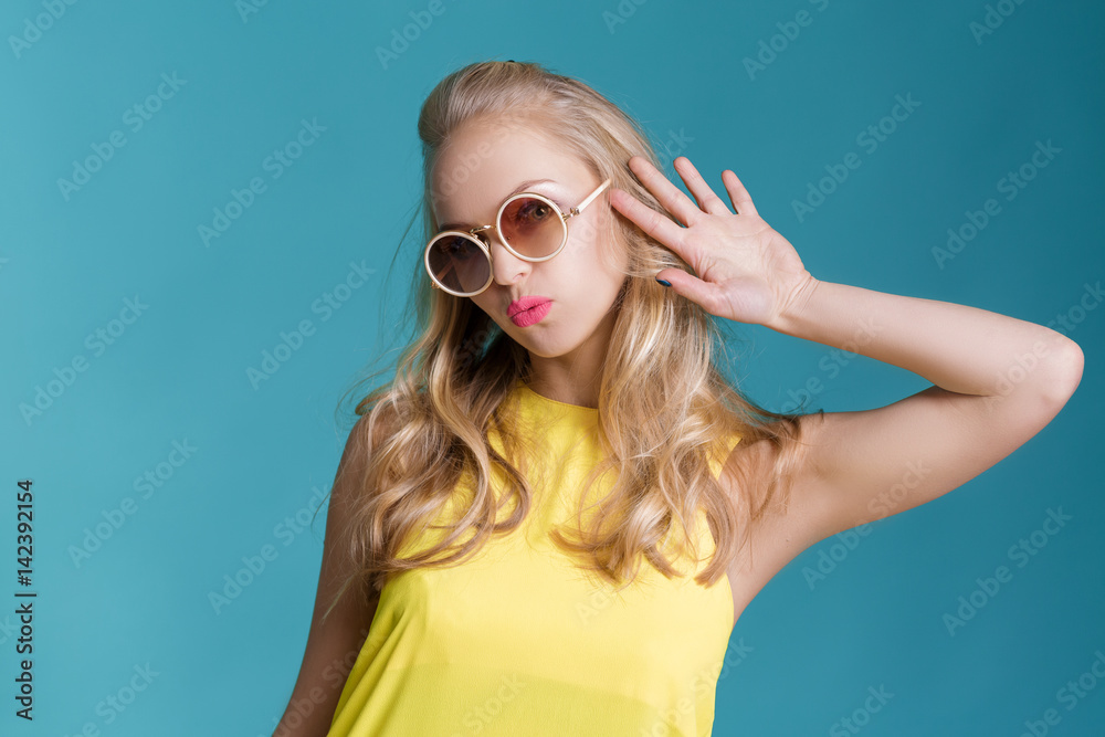 portrait of beautiful blond woman in sunglasses and yellow shirt on blue background. Carefree summer.