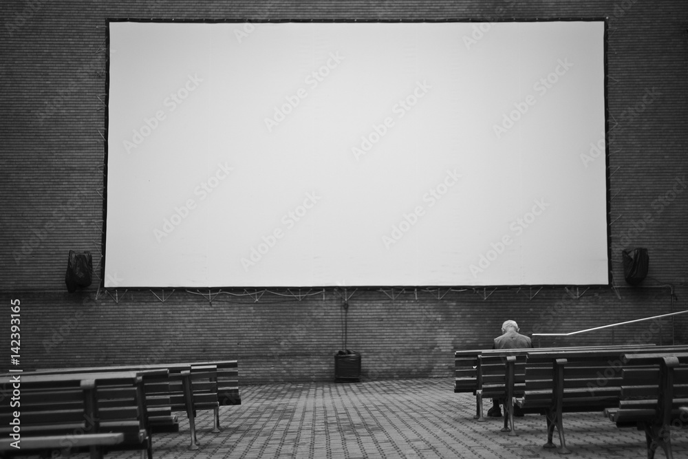 Outdoor projection movie screen with benches and a person head down in the first row