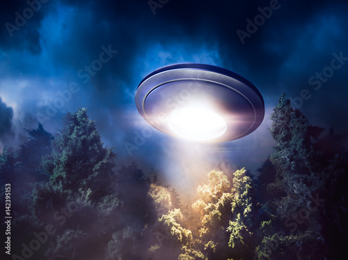 Photography High contrast image of UFO flying over a forest with light beam at night