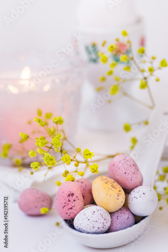 Chocolate Easter eggs in pastel colors in ceramic spoon, burning candle, white napkin, elegant table setting