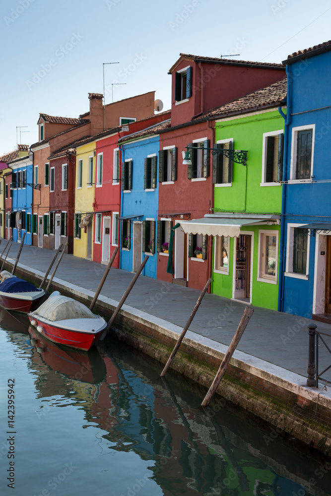 A row of several brightly coloured buildings on the ede of a canal in Burano Italy